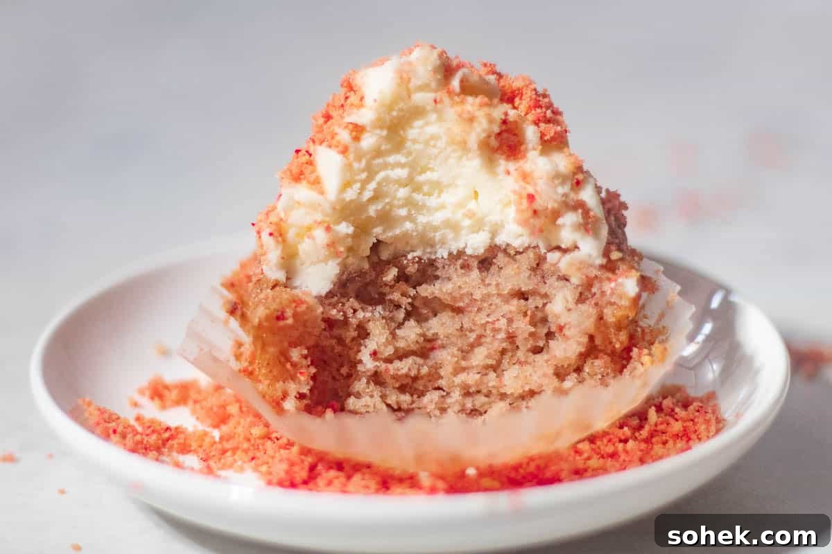 Strawberry Crunch Cupcakes Recipe with Crispy Topping 14 Close-up of a half-eaten strawberry crunch cupcake revealing its moist texture, with crumbs scattered on a white plate.