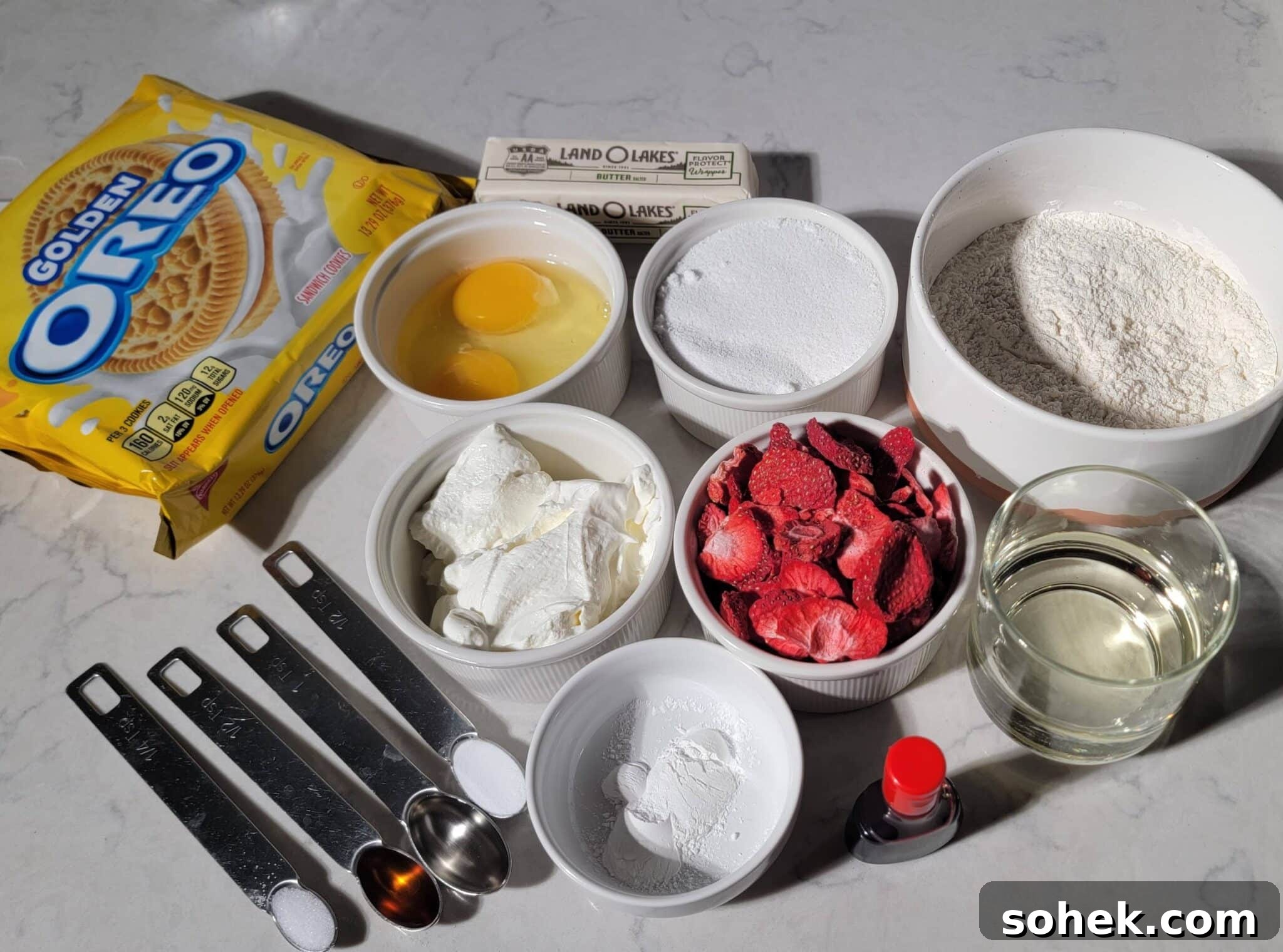 Strawberry Crunch Cupcakes Recipe with Crispy Topping 4 Ingredients for strawberry crunch cupcakes, featuring Golden Oreos, butter, eggs, flour, sugar, and freeze-dried strawberries on a marble counter.