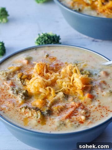 broccoli cheese soup in a blue bowl with a spoon, with broccoli scattered around