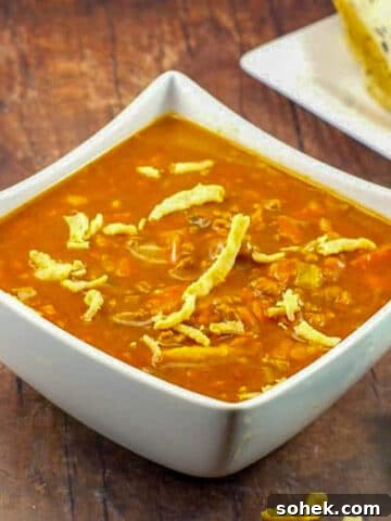 Carrot Tomato Soup in white bowl on brown wooden surface, with bread in background
