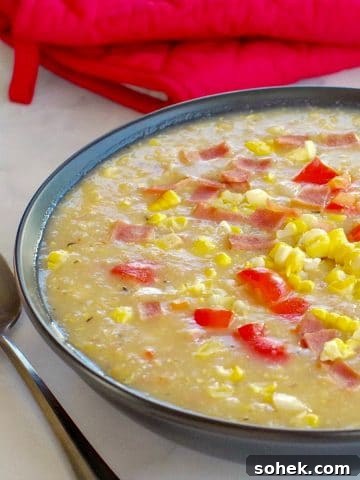Healthy Corn Chowder in a black bowl, with a spoon on the side and red over mitts in background