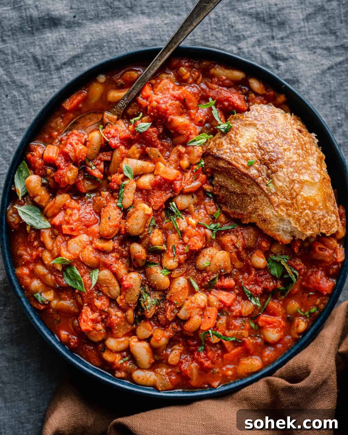 livornese stewed beans in a bowl bowl with a piece of bread on blue tablecloth