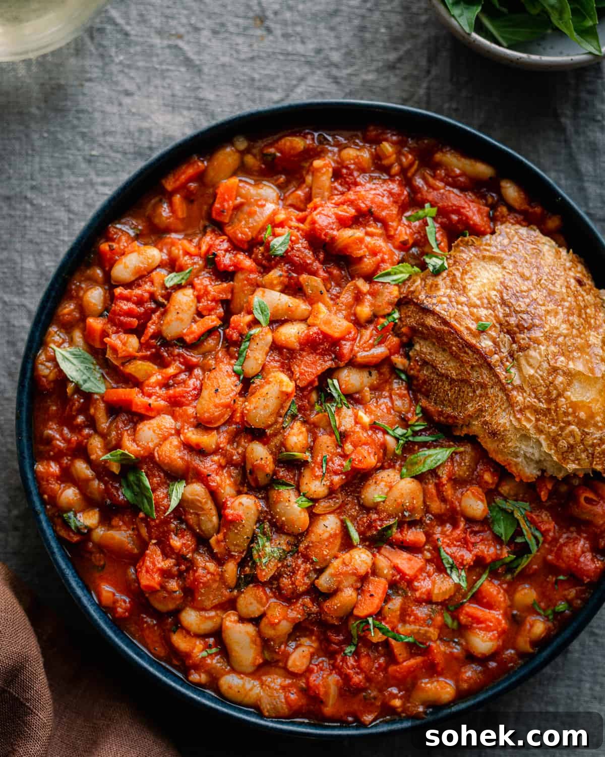 livornese stewed beans in a bowl bowl with a piece of bread on blue tablecloth