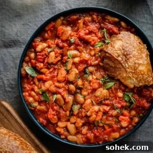 livornese stewed beans in a bowl bowl with a piece of bread on blue tablecloth.
