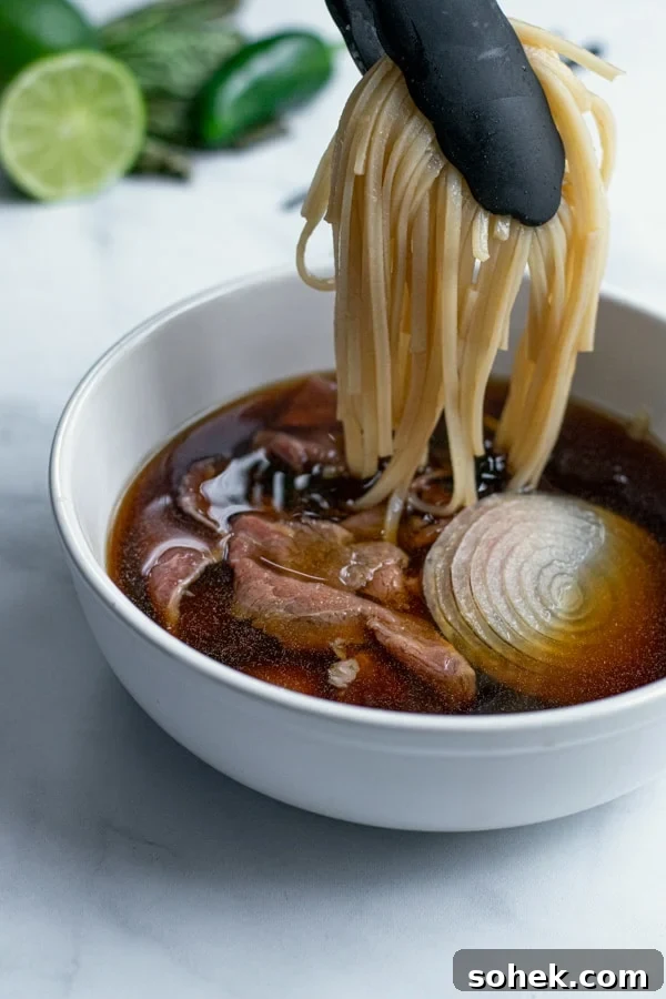 noodles being placed into the soup bowl with a pair of tongs