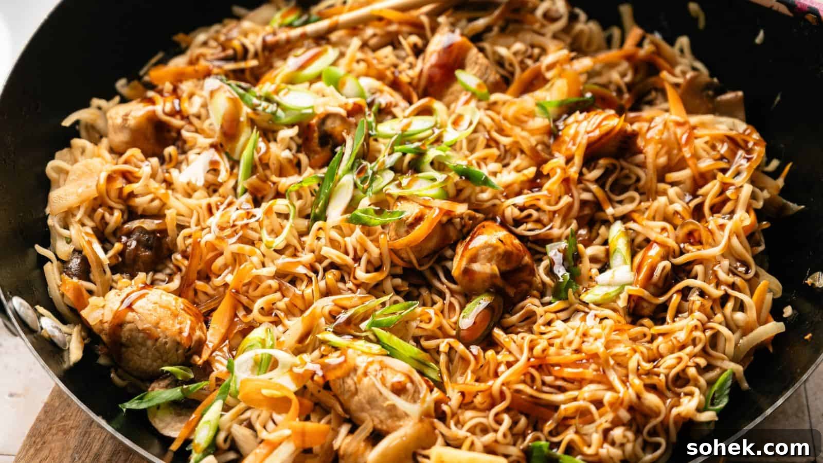 33 Quick Chicken Dinners for Busy Nights When You’re Tired but Hungry 24 A close-up of cooked stir-fried noodles with pieces of chicken, sliced carrots, green onions, and a savory sauce in a black pan.
