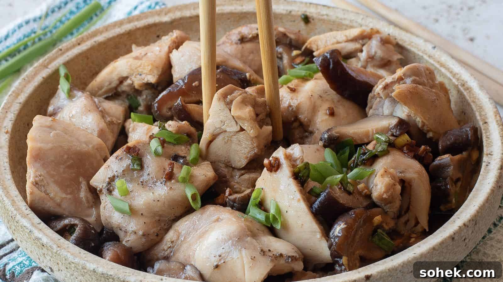 33 Quick Chicken Dinners for Busy Nights When You’re Tired but Hungry 5 A bowl of steamed chicken pieces with mushrooms, garnished with chopped green onions, with chopsticks picking up a piece.