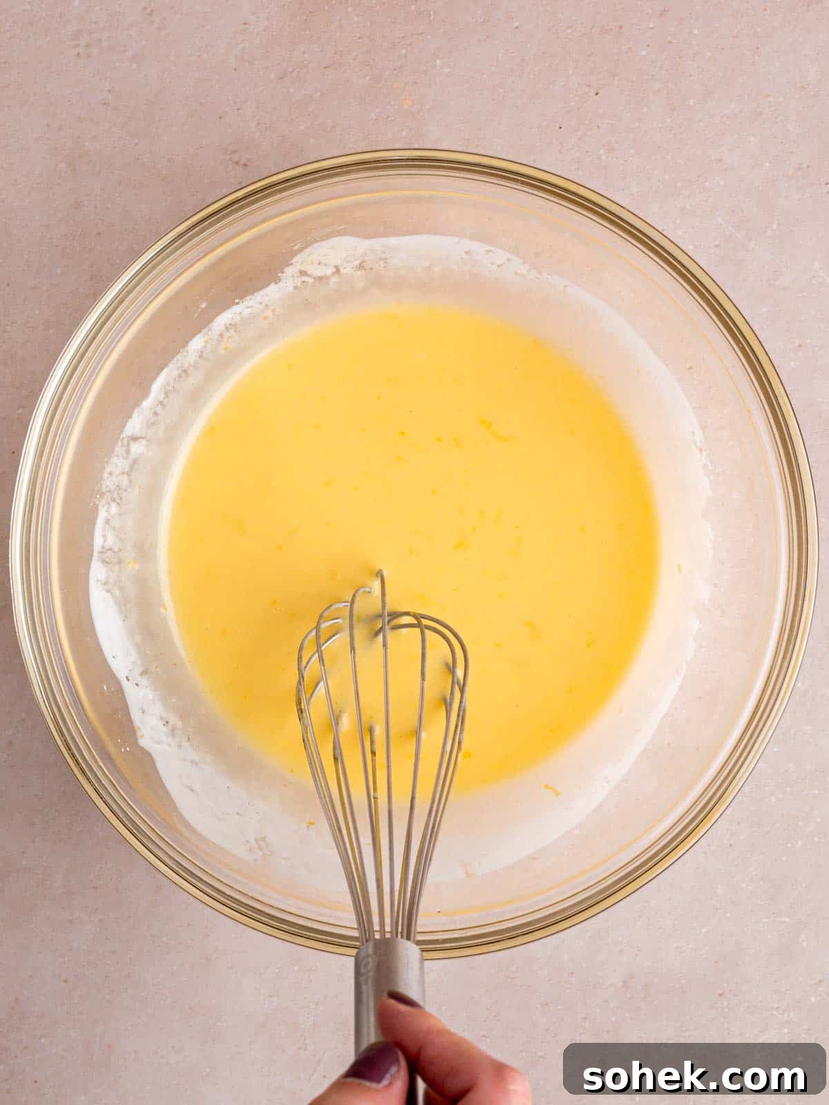 Whisking vegetable oil, sugar, lemon zest, egg, vanilla extract, and lemon kefir in a bowl.