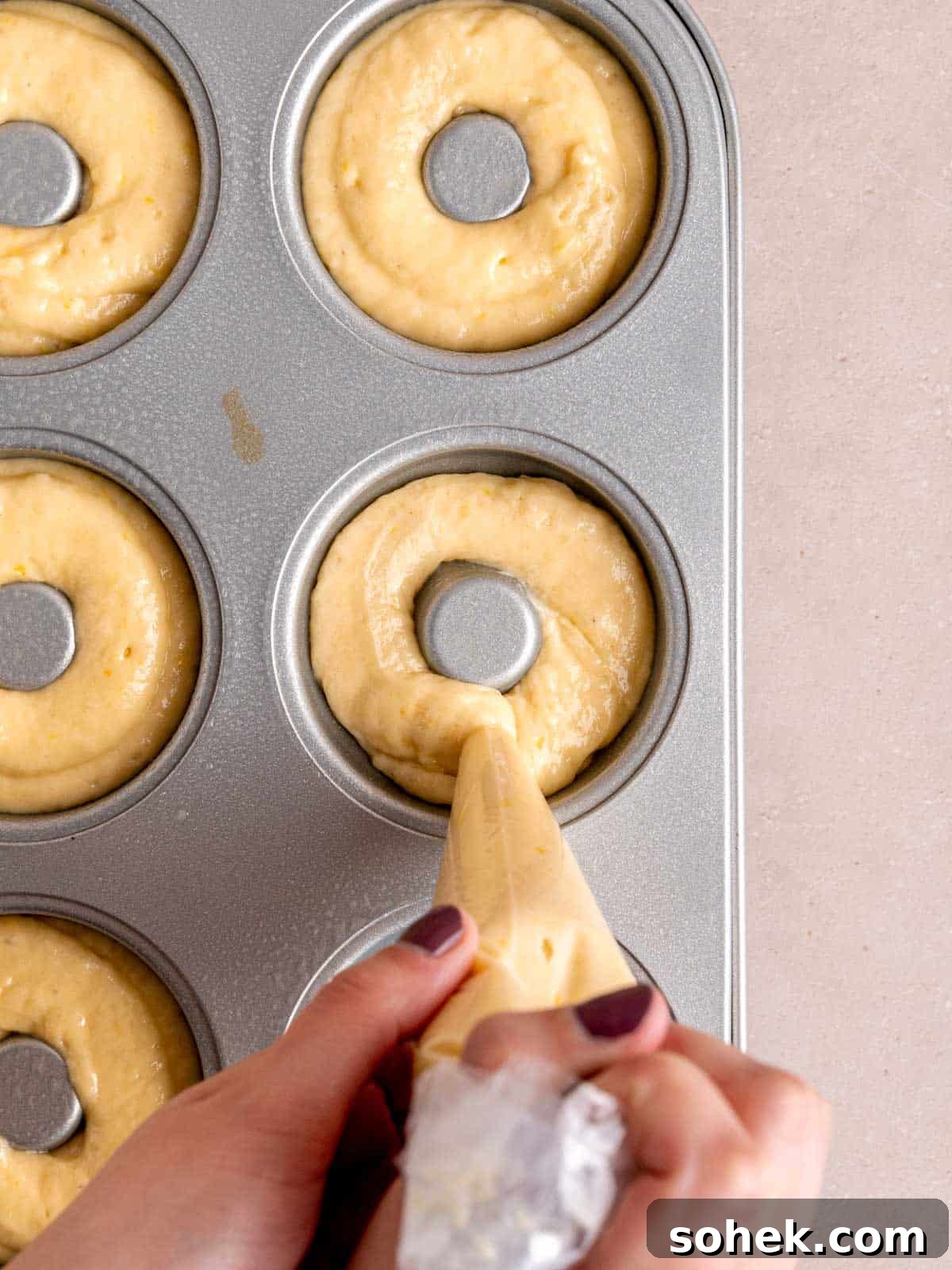 Piping lemon cake batter into a donut pan.
