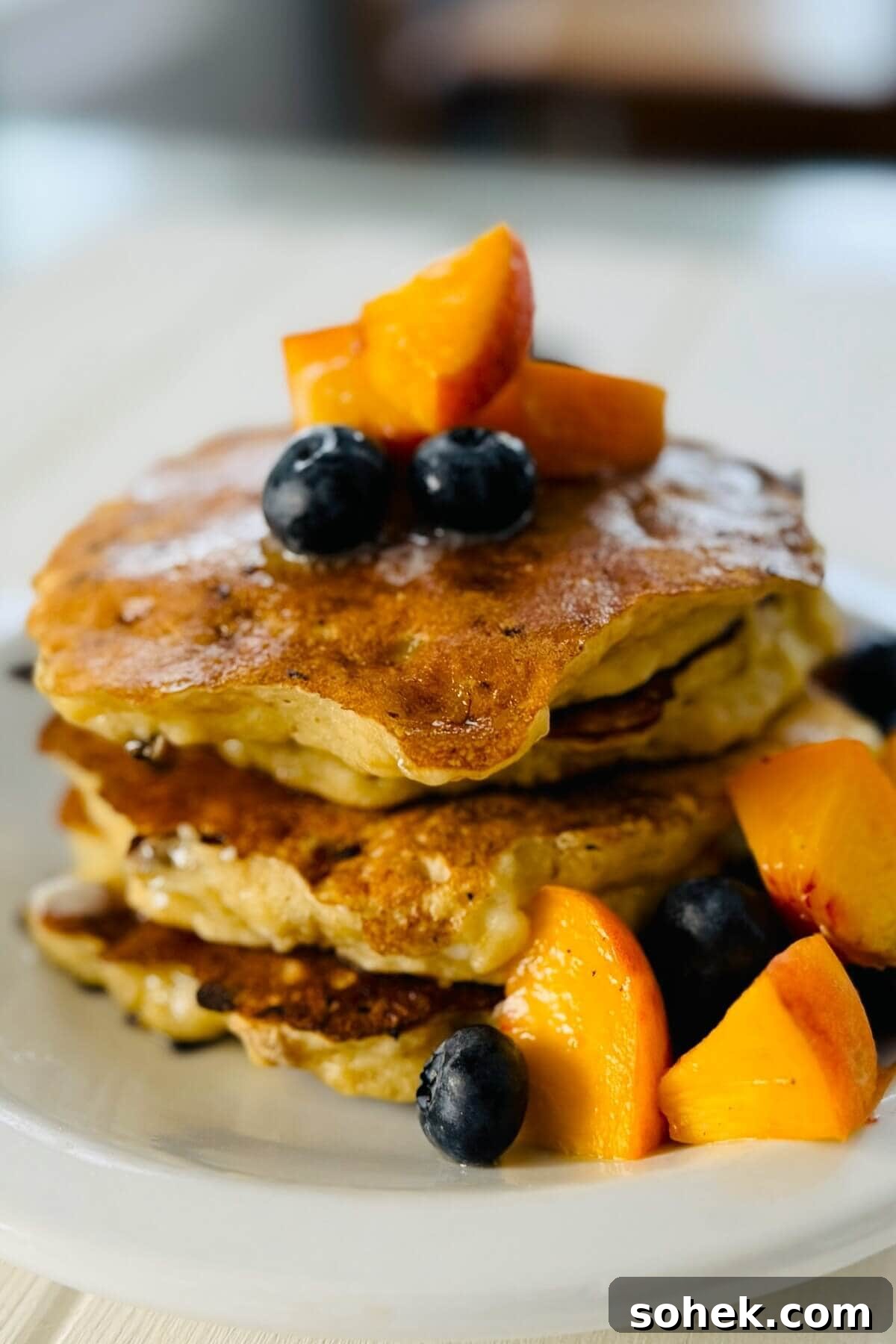 Fluffy Banana and Cottage Cheese Pancakes for Protein-Packed Breakfast 2 Stack of 3 protein pancakes with bananas with peaches and blueberries.