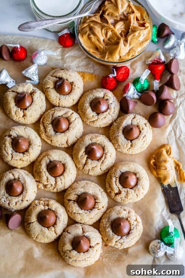 overhead shot of about a dozen peanut butter kiss cookies, a bowl of peanut butter, and Hershey's kisses.