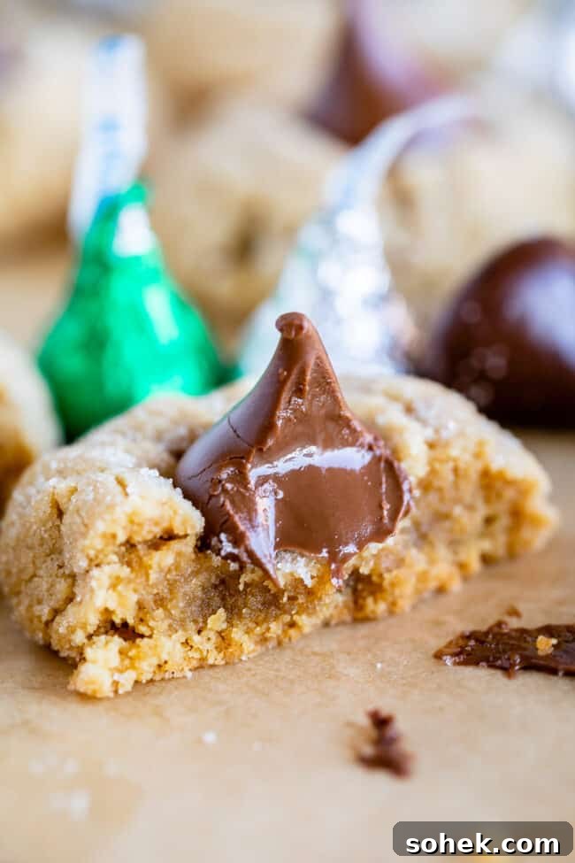 peanut butter kiss cookie with bite taken out and more Hershey's kisses in the background.