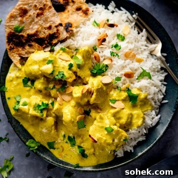 Chicken pasanda and rice on a dark plate with a piece of chapati on the plate.