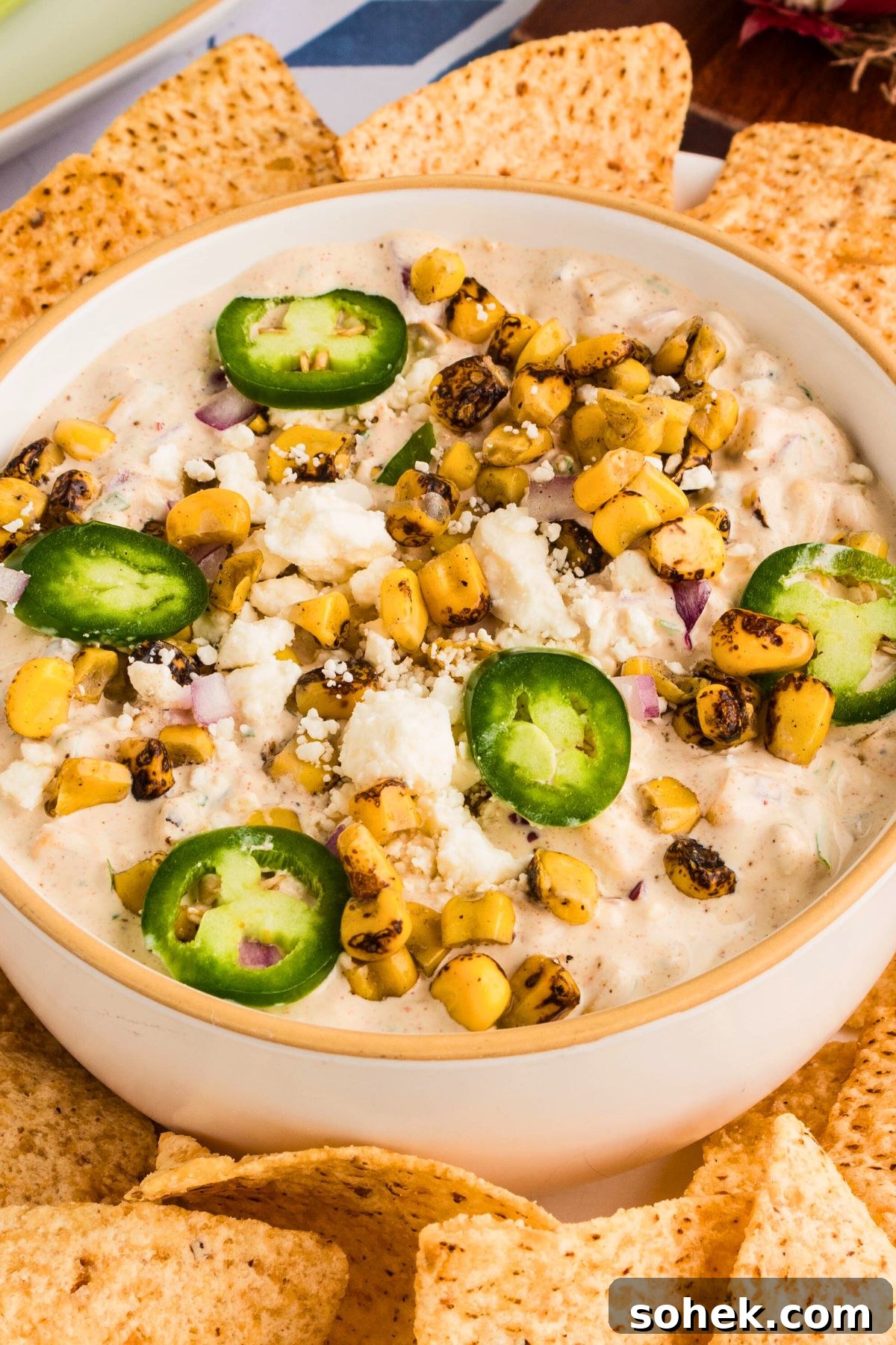 Creamy Mexican street corn dip in a white bowl surrounded by tortilla chips. 