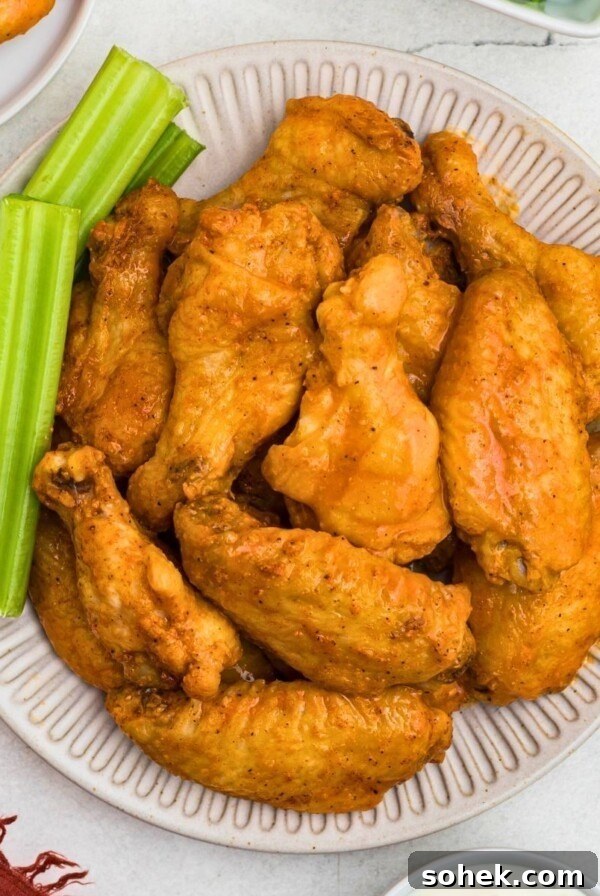 Crispy baked chicken wings, tossed in buffalo sauce, on a white plate with celery sticks on the plate.