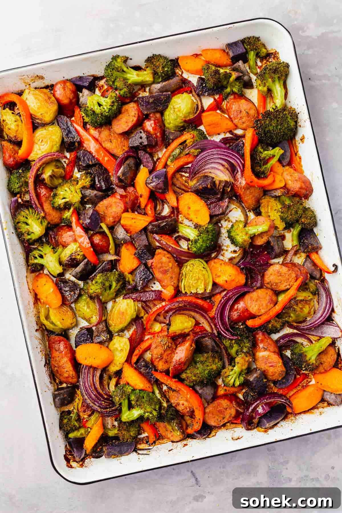 Sheet Pan Sausage and Roasted Vegetables with Herbs 2 An overhead view of roasted sausage and vegetables on a white sheet pan after baking.