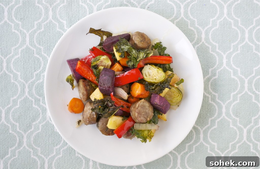 Sheet Pan Sausage and Roasted Vegetables with Herbs 15 Roasted sausage, purple sweet potato, red bell peppers, brussels sprouts, carrots and kale on a white plate.