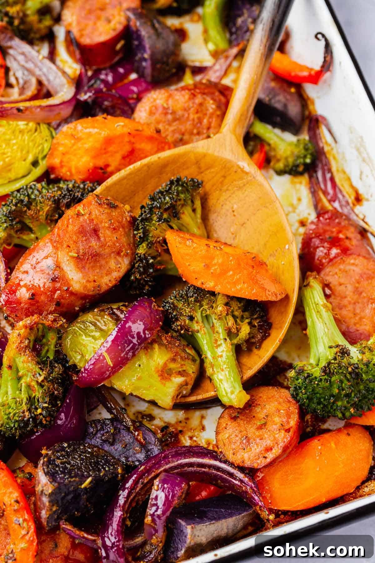 Sheet Pan Sausage and Roasted Vegetables with Herbs 10 A wood spoon scooping up roasted sausage and vegetables from a sheet pan.