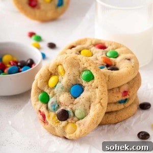 Chewy M&M Cookies Recipe for Perfect Chocolate Crumble 12 Stack of 4 m&m cookies on a piece of parchment paper with another cookie leaning against the stack.