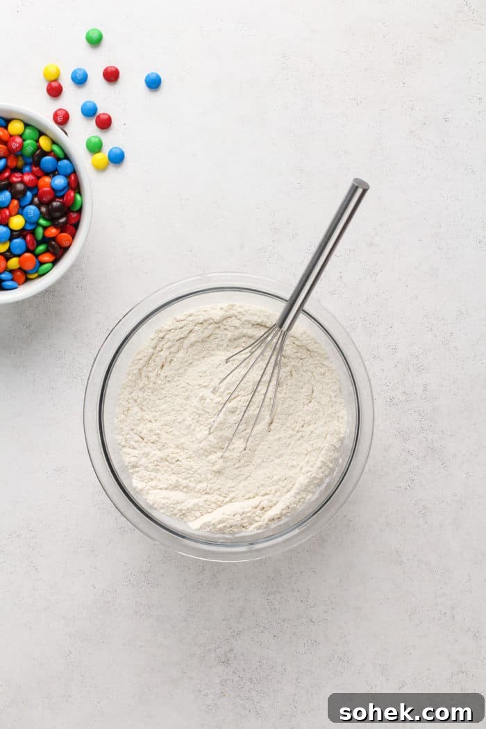 Chewy M&M Cookies Recipe for Perfect Chocolate Crumble 4 Dry ingredients for M&M cookies being whisked together in a glass bowl.