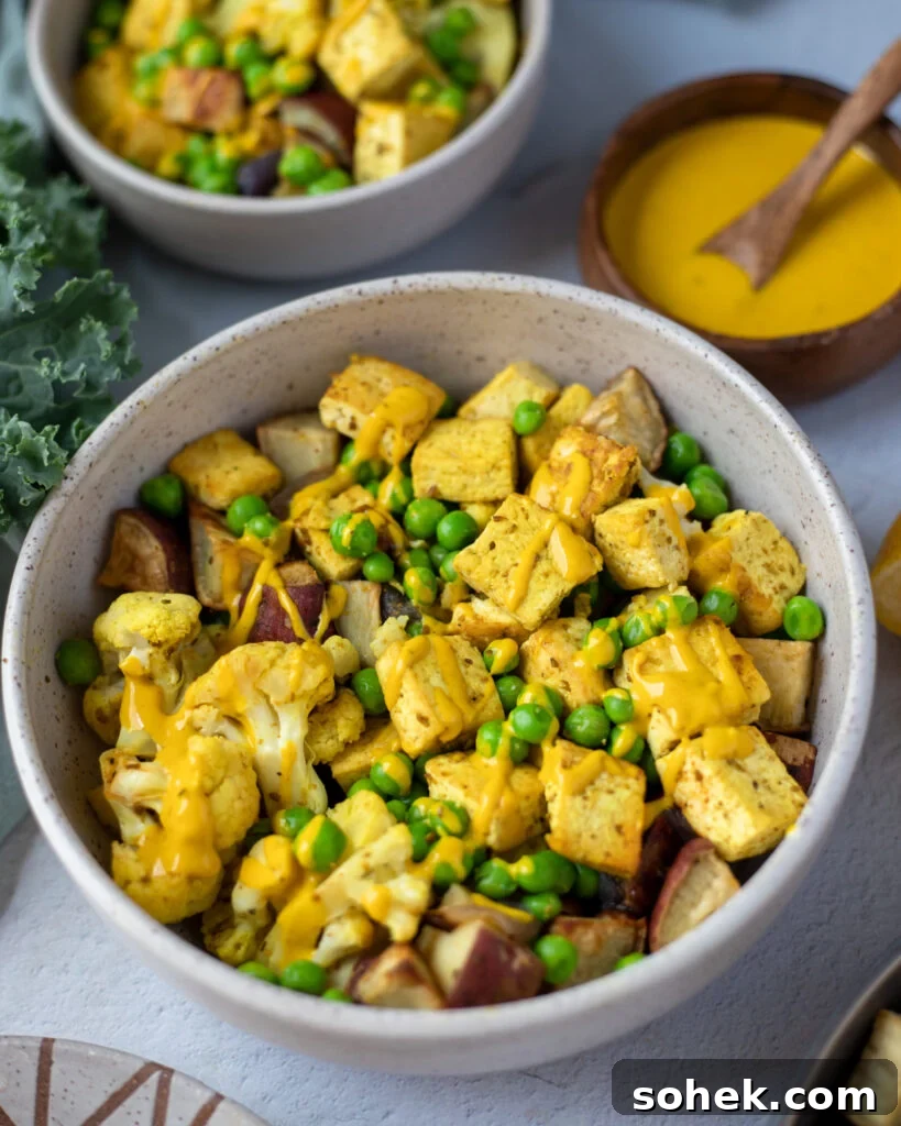 overhead view of a white bowl with curry tofu salad with turmeric tahini drizzle next to fresh kale and a bowl of the drizzle.