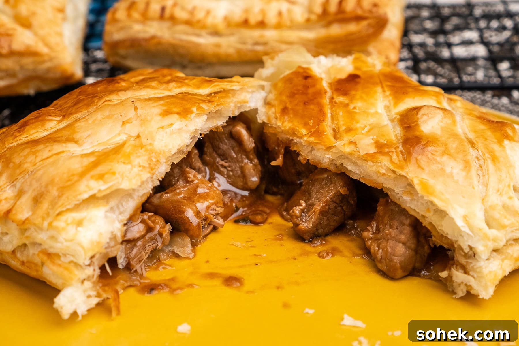 Greggs-Style Steak Bake Recipe: How to Make It at Home 3 A steak bake that has been torn in half with the beef filling and gravy pouring out onto a plate