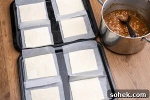 Greggs-Style Steak Bake Recipe: How to Make It at Home 17 A large pot of steak bake filling with eight squares of puff pastry on parchment paper on two baking trays