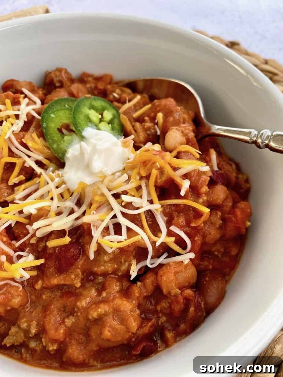 Classic Idaho Chili Recipe: Hearty Potato and Beef Chili 10 A bowl of chili with shredded cheese, sour cream and jalapenos on top with a spoon on the side