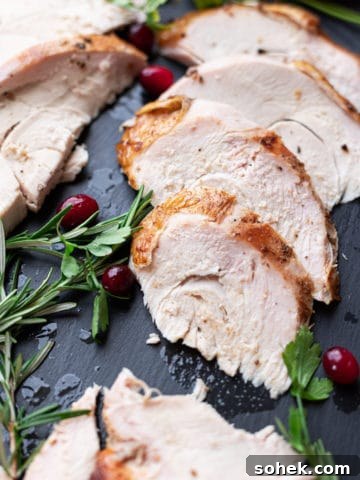 Sliced turkey on a platter, rosemary and cranberries on side.