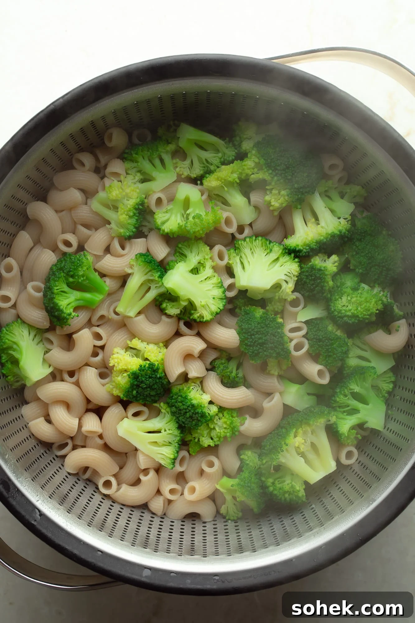 High-Protein Sharp White Mac and Cheese with Broccoli 4 overhead view of a cooked pasta and broccoli in a colander.