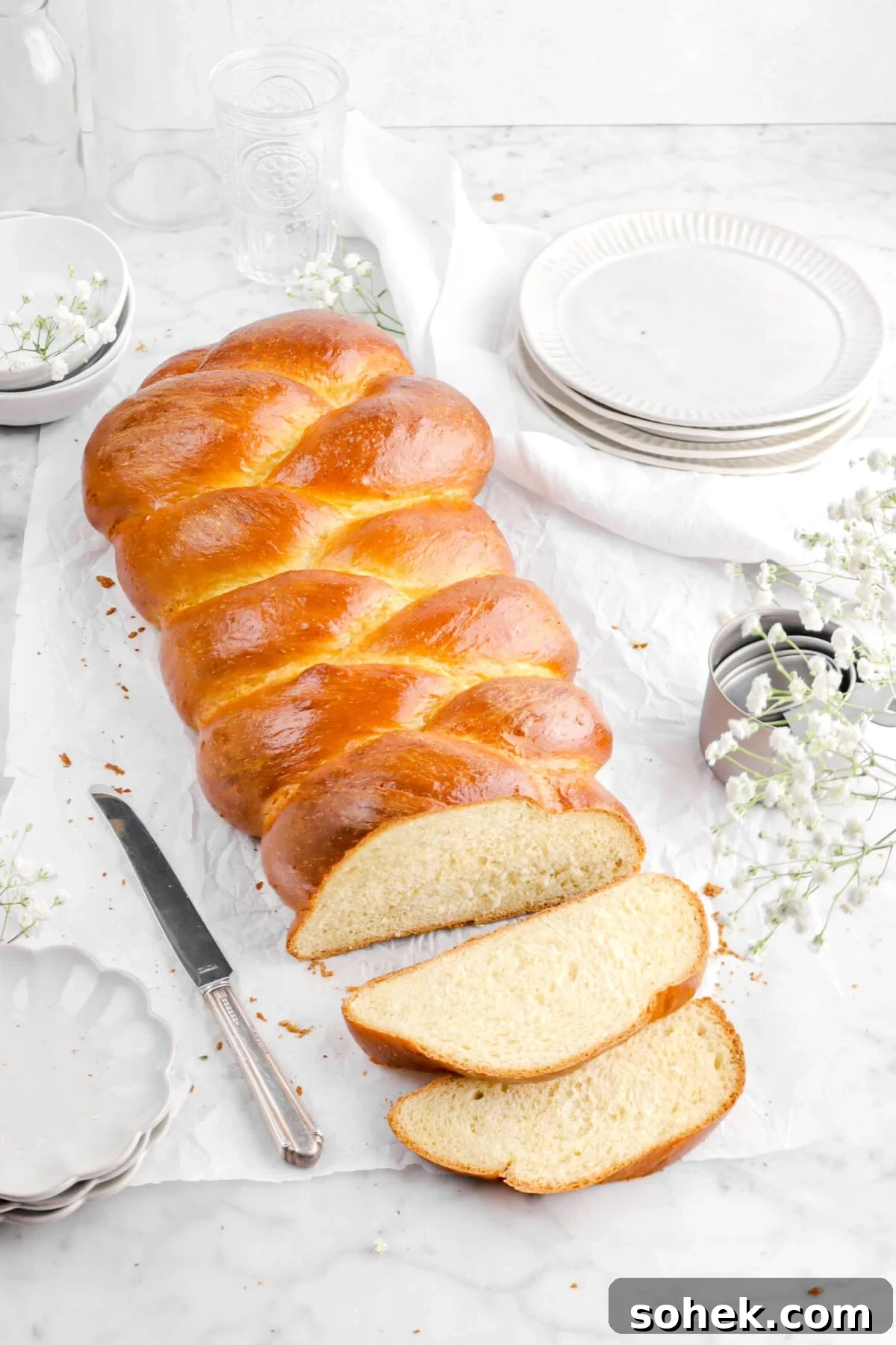 angled shot of challah with two slices laying in front with plates, flowers, and a knife