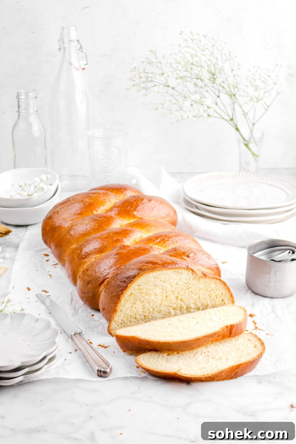 challah with two slices laying in front, flowers, plates, bowls, and empty glasses behind