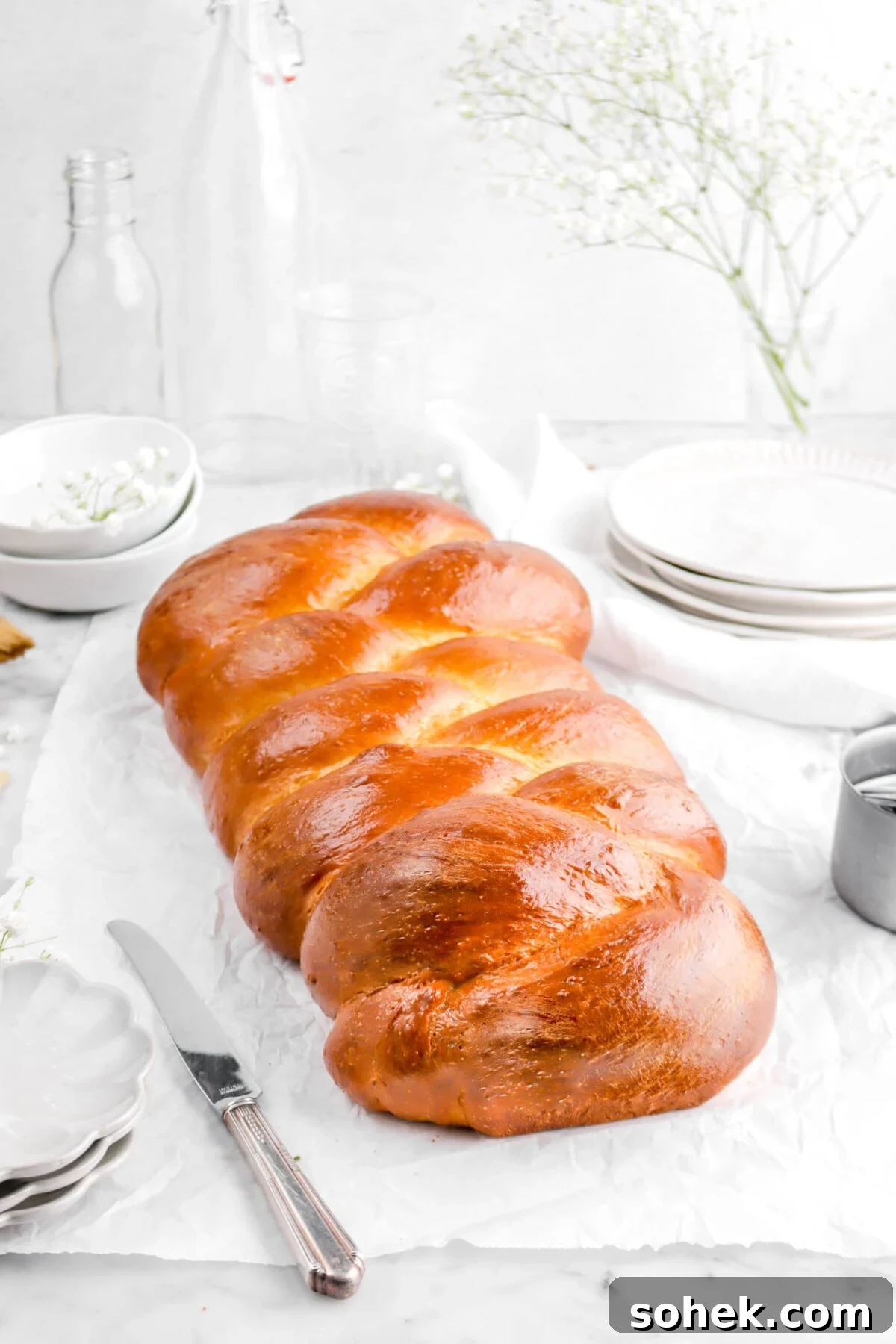 front shot of challah on parchment paper with plates, bowls, and glasses behind