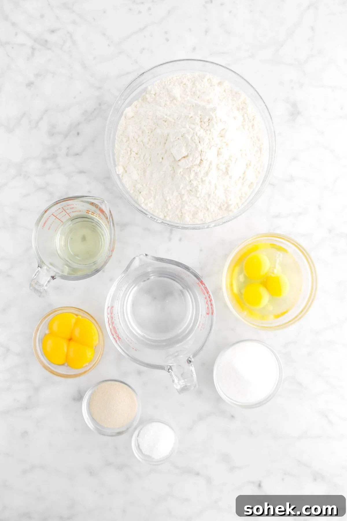 flour, oil eggs, water, egg yolks, yeast, salt, and sugar on marble surface