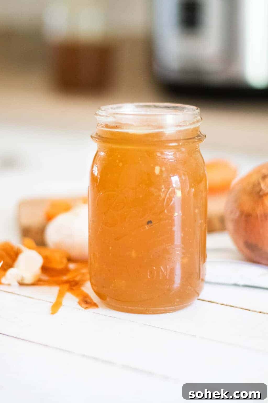 Homemade bone broth in mason jar with carrots and onions on table.