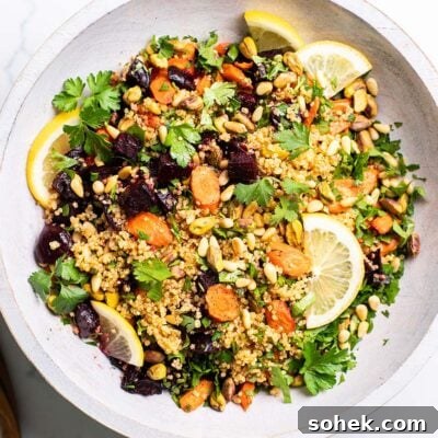 A colorful quinoa salad shown served in a white bowl with a wooden spoon.