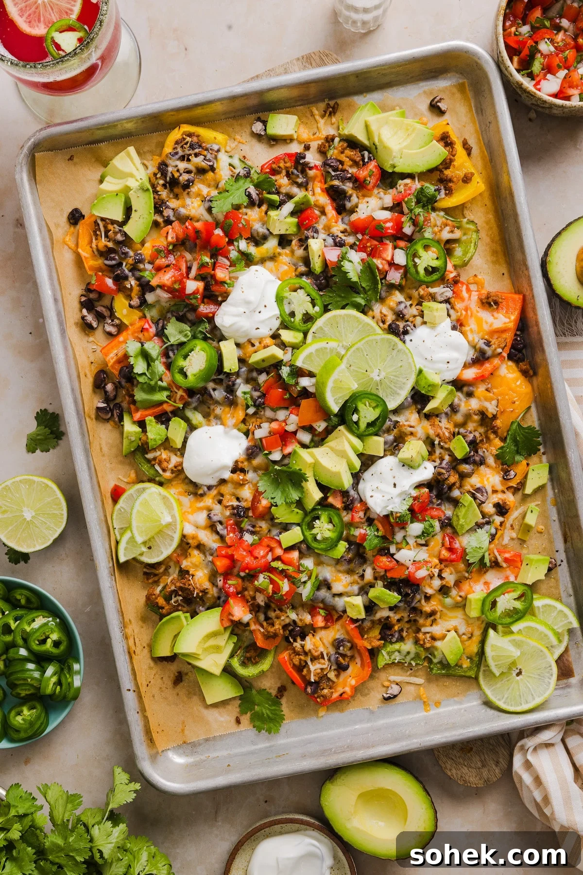 Bell pepper nachos made with nutritious ingredients like bell peppers, lean meat and beans and topped with your favorite nacho toppings. Bell pepper nachos on a sheet pan with nacho toppings and sour cream.