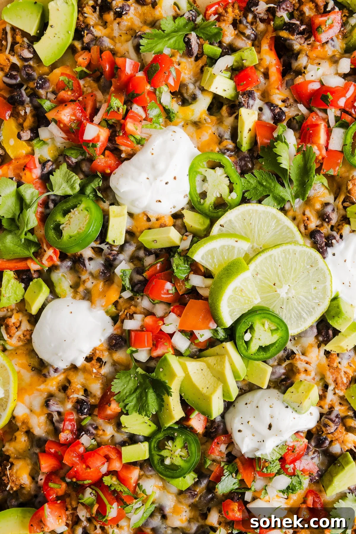 Bell pepper nachos made with nutritious ingredients like bell peppers, lean meat and beans and topped with your favorite nacho toppings. A close up shot of bell pepper nachos on a sheet pan with nacho toppings and sour cream.