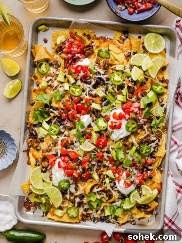A baking sheet filled with ground turkey nachos loaded with avocado, jalapenos, tomatoes and more.