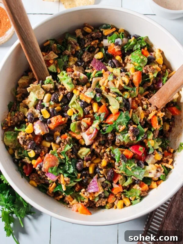 A chopped taco ground beef salad tossed with dressing in a white bowl.