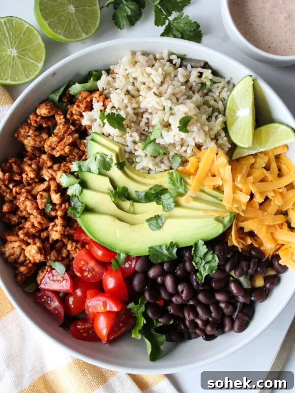 A taco rice bowl with ground turkey, rice, avocado, tomato, black beans, and shredded cheese with a creamy taco dressing on the side.