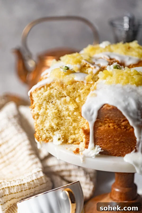 sliced pineapple pound cake on a cake stand covered in a pineapple glaze and topped with crushed pineapples.