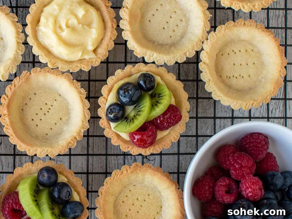 Mini Fresh Fruit Tarts Recipe: Bite-Sized Dessert for Parties 14 Overhead view of mini tarts, some empty, some filled with pastry cream and some topped with berries and sliced kiwi fruit.