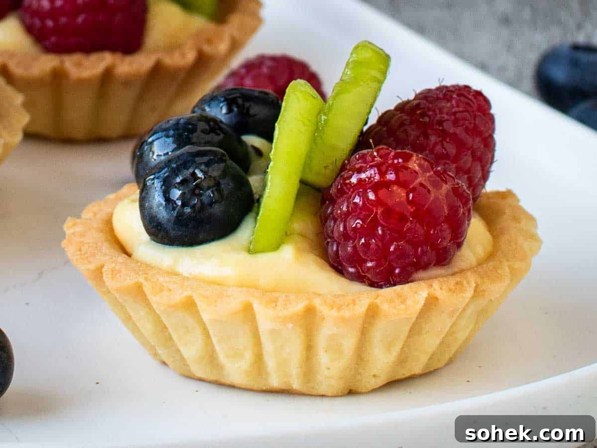 Mini Fresh Fruit Tarts Recipe: Bite-Sized Dessert for Parties 15 Close up of fluted tart filled with pastry cream and topped with blueberries, sliced kiwi fruit and raspberries