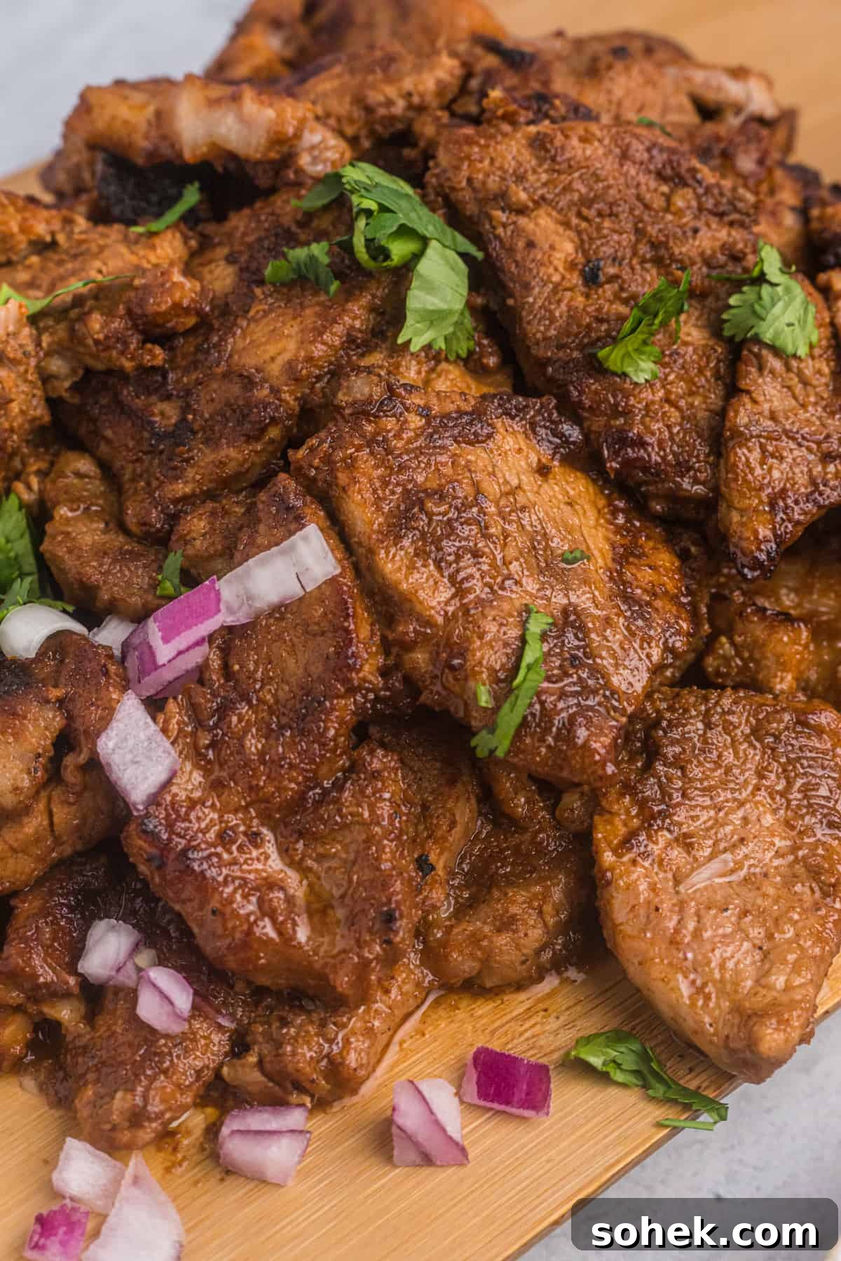 Cooked pork is topped with red onions and cilantro. 