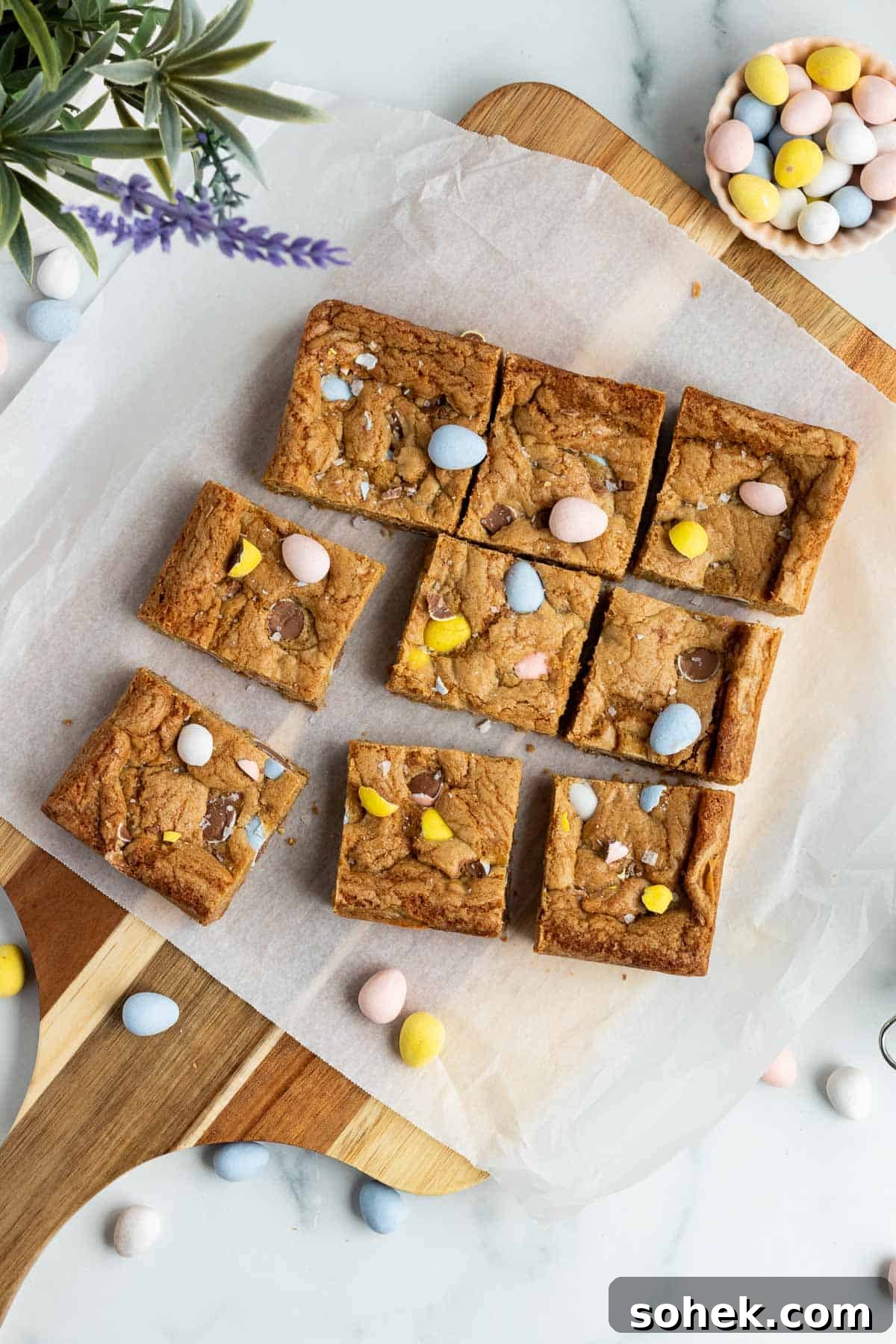 Mini Egg Cookie Bars Recipe — Chewy Springtime Treat 2 mini egg cookie bars cut into squares sitting on a cutting board with parchment paper on top
