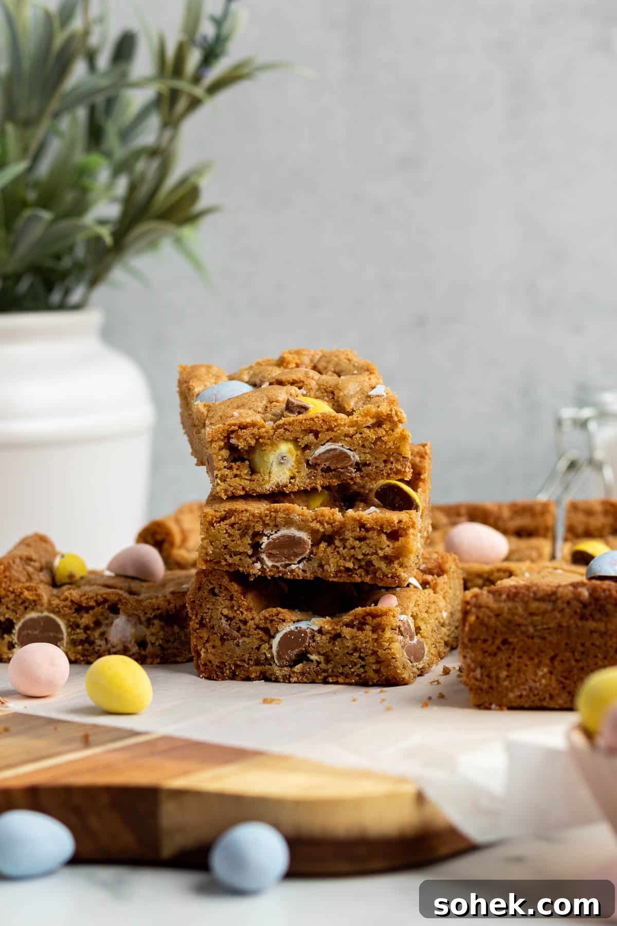 Mini Egg Cookie Bars Recipe — Chewy Springtime Treat 4 a stack of 3 mini egg cookie bars with a white vase of flowers in the background