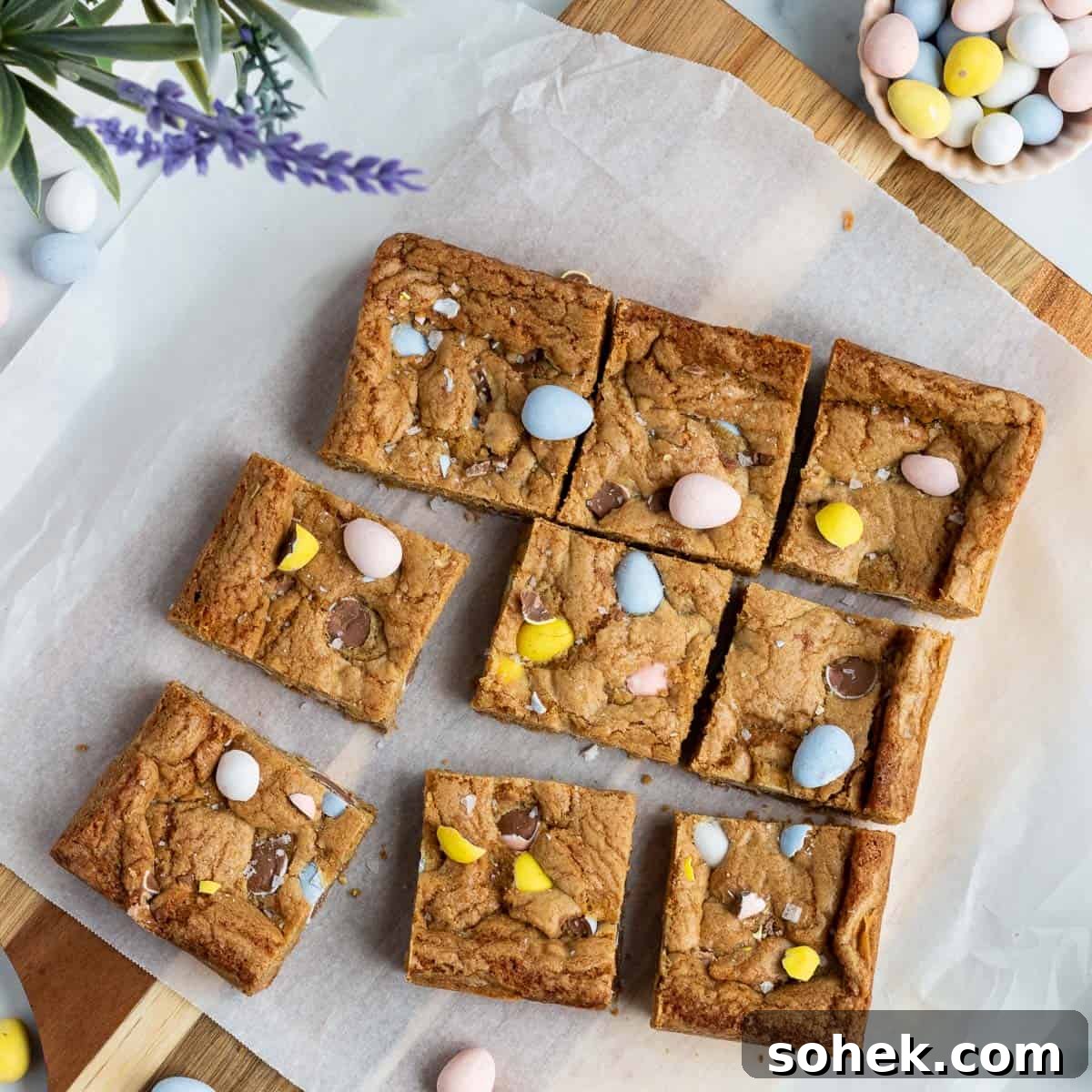 mini egg cookie bars cut into squares sitting on a cutting board with parchment paper on top