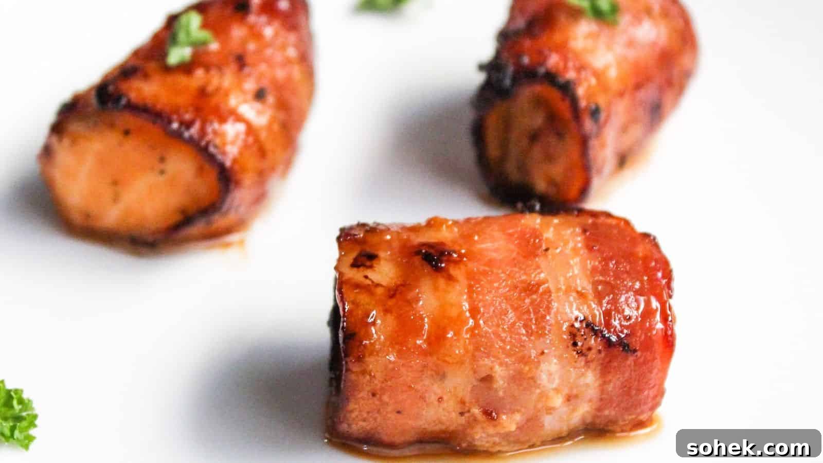26 Irresistible Air Fryer Game Day Snacks to Serve Guests 3 Three pieces of bacon-wrapped salmon bites garnished with parsley on a white plate.