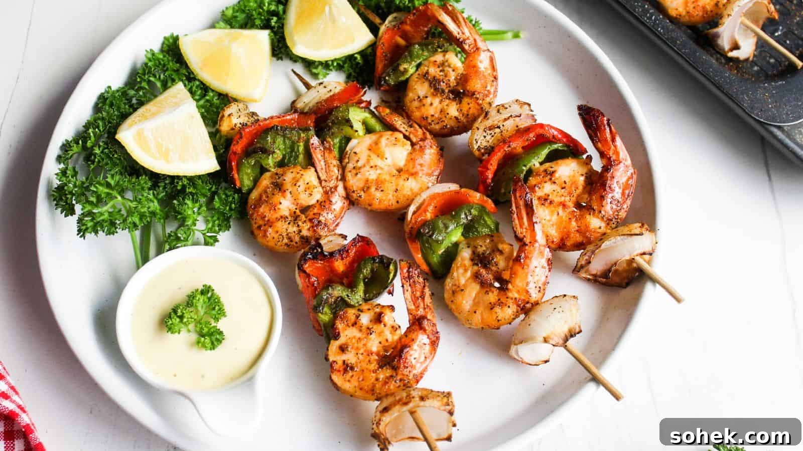 26 Irresistible Air Fryer Game Day Snacks to Serve Guests 25 Grilled shrimp skewers with red and green bell peppers, served with lemon wedges and a dipping sauce on a white plate.